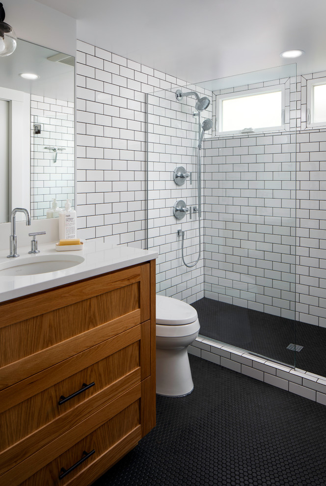 Inspiration for a mid-sized modern bathroom in Portland with recessed-panel cabinets, medium wood cabinets, a one-piece toilet, white tile, ceramic tile, white walls, ceramic floors, an undermount sink, engineered quartz benchtops, black floor, a hinged shower door and white benchtops.