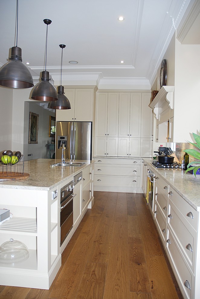 Design ideas for a large traditional l-shaped eat-in kitchen in Sydney with a double-bowl sink, shaker cabinets, white cabinets, granite benchtops, white splashback, subway tile splashback, stainless steel appliances, medium hardwood floors and with island.