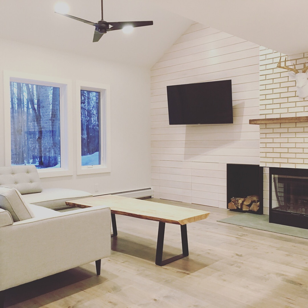 Inspiration pour un salon minimaliste en bois de taille moyenne et fermé avec un mur blanc, parquet clair, une cheminée d'angle, un manteau de cheminée en brique, un téléviseur fixé au mur et un plafond voûté.