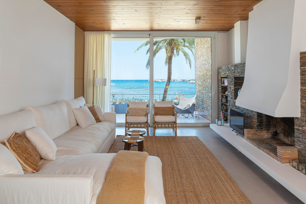 Modelo de sala de estar abierta mediterránea extra grande con paredes blancas, suelo de cemento, todas las chimeneas, marco de chimenea de piedra y suelo gris