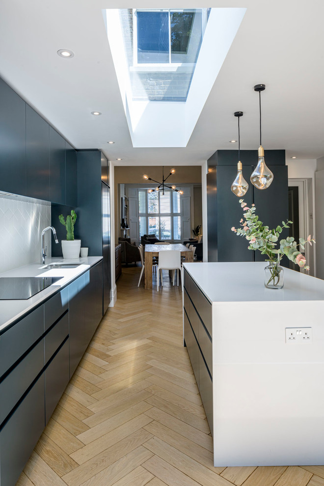 Inspiration for a contemporary galley kitchen in London with flat-panel cabinets, grey cabinets, solid surface benchtops, white splashback, ceramic splashback, light hardwood floors, white benchtop, with island and beige floor.