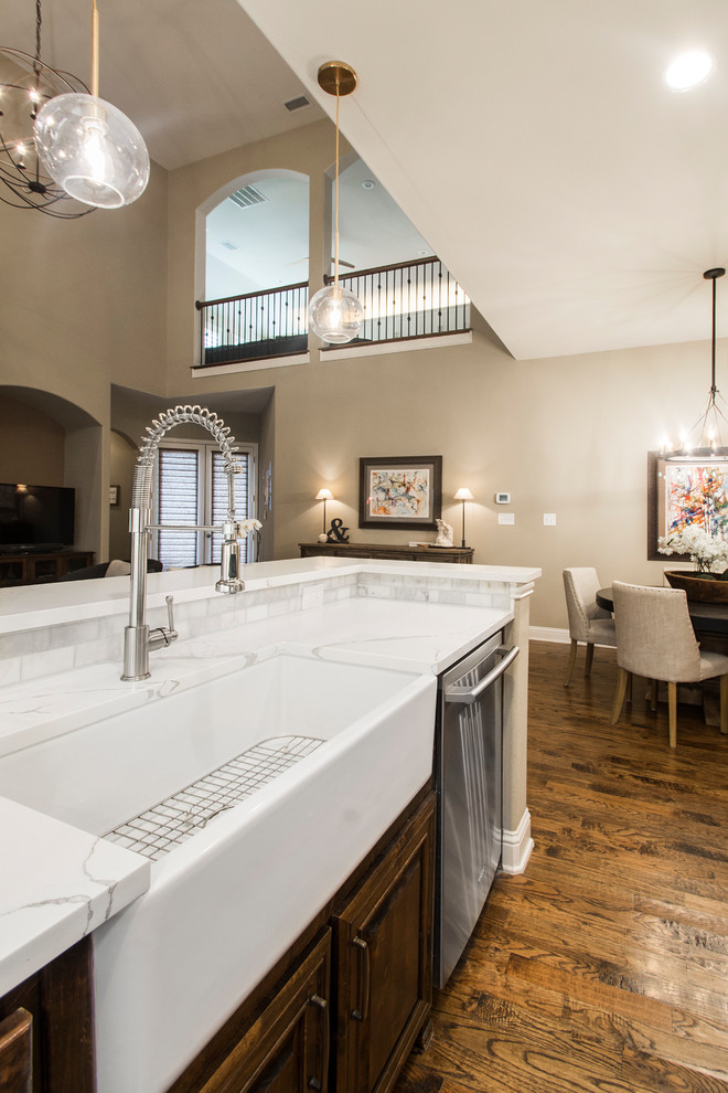 Photo of a large transitional u-shaped eat-in kitchen in Dallas with a farmhouse sink, raised-panel cabinets, dark wood cabinets, quartz benchtops, grey splashback, marble splashback, stainless steel appliances, medium hardwood floors, with island, brown floor and white benchtop.