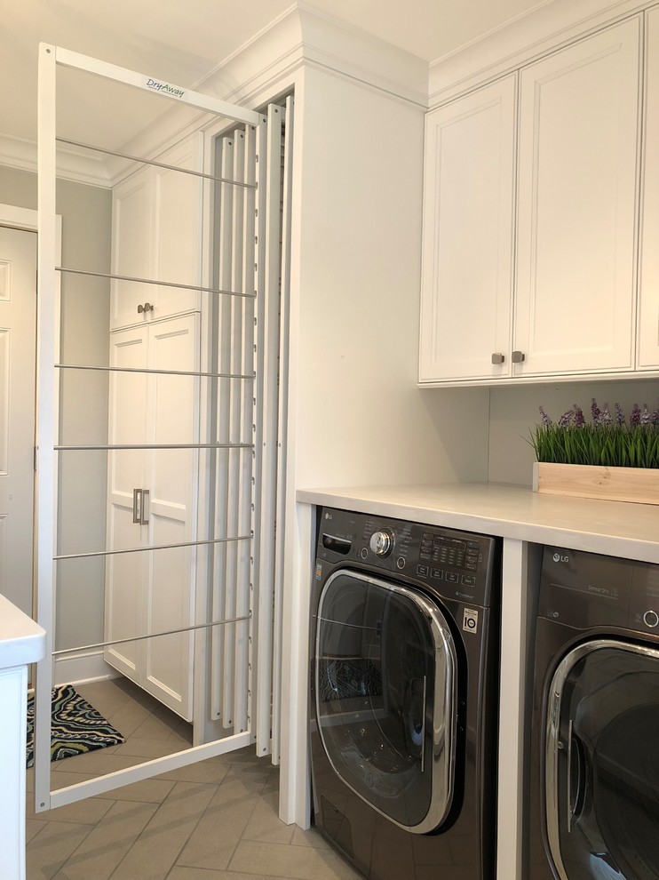 Inspiration for a mid-sized transitional galley utility room in Milwaukee with a farmhouse sink, recessed-panel cabinets, white cabinets, grey walls, ceramic floors, a concealed washer and dryer, brown floor and grey benchtop.