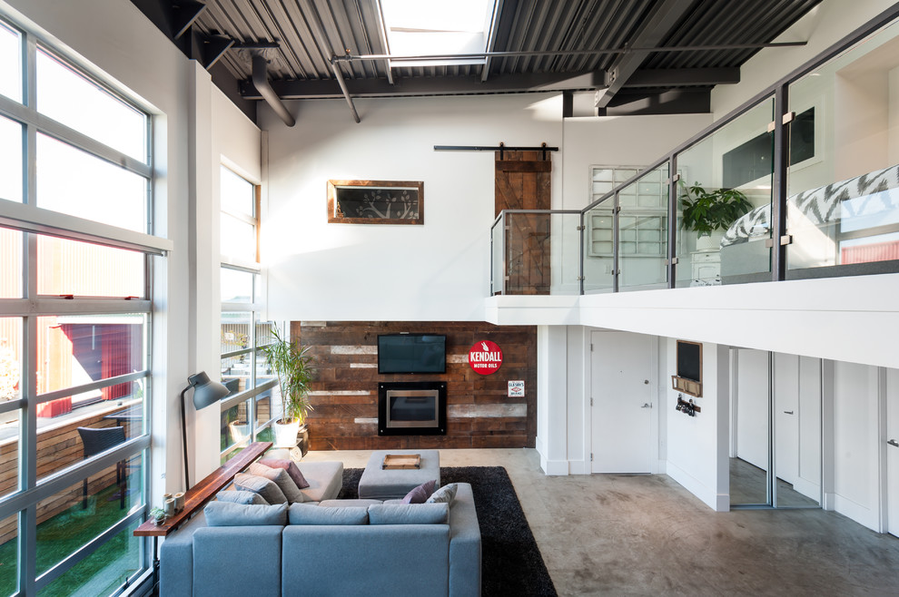 This is an example of a large industrial open concept living room in Vancouver with white walls, concrete floors, a ribbon fireplace and a wall-mounted tv.
