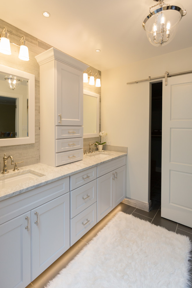 Photo of a mid-sized transitional master bathroom in Chicago with flat-panel cabinets, white cabinets, an open shower, a one-piece toilet, gray tile, stone tile, white walls, ceramic floors, an undermount sink, marble benchtops, black floor and an open shower.
