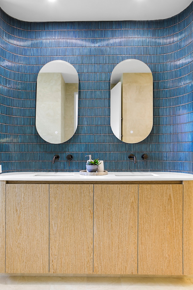 На фото: ванная комната среднего размера в современном стиле с плоскими фасадами, светлыми деревянными фасадами, унитазом-моноблоком, синей плиткой, керамической плиткой, бежевыми стенами, полом из керамической плитки, врезной раковиной, столешницей из искусственного кварца, бежевым полом, открытым душем, белой столешницей, тумбой под две раковины и встроенной тумбой