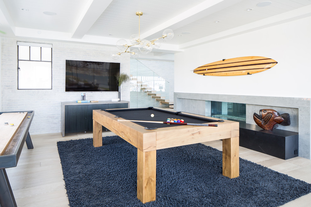 Photo of a beach style family room in Orange County with a game room, white walls, light hardwood floors, a ribbon fireplace, a wall-mounted tv and beige floor.