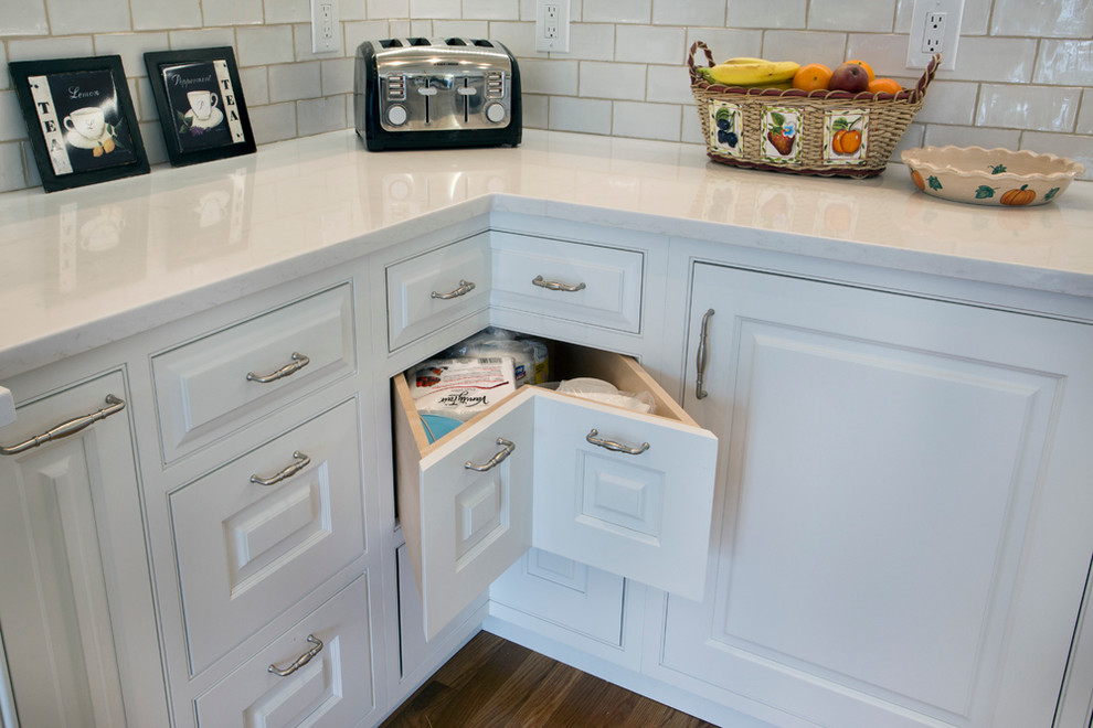 Inspiration for a large transitional l-shaped medium tone wood floor eat-in kitchen remodel with a farmhouse sink, white cabinets, granite countertops, white backsplash, stainless steel appliances, an island, raised-panel cabinets and subway tile backsplash