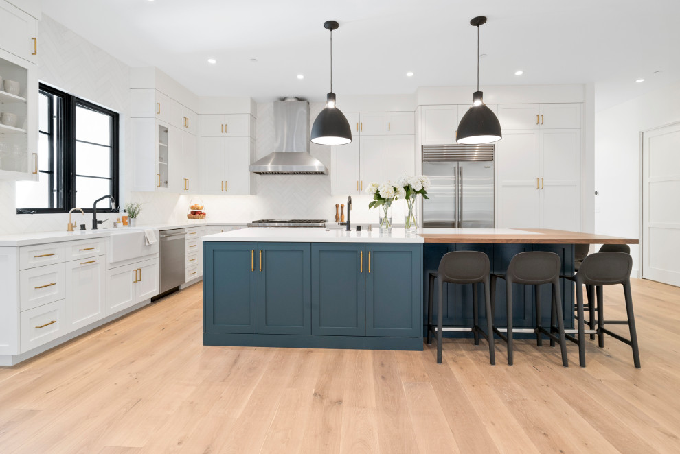 Design ideas for a mid-sized country l-shaped separate kitchen in San Francisco with a farmhouse sink, shaker cabinets, white cabinets, white splashback, stainless steel appliances, light hardwood floors, with island, brown floor and white benchtop.