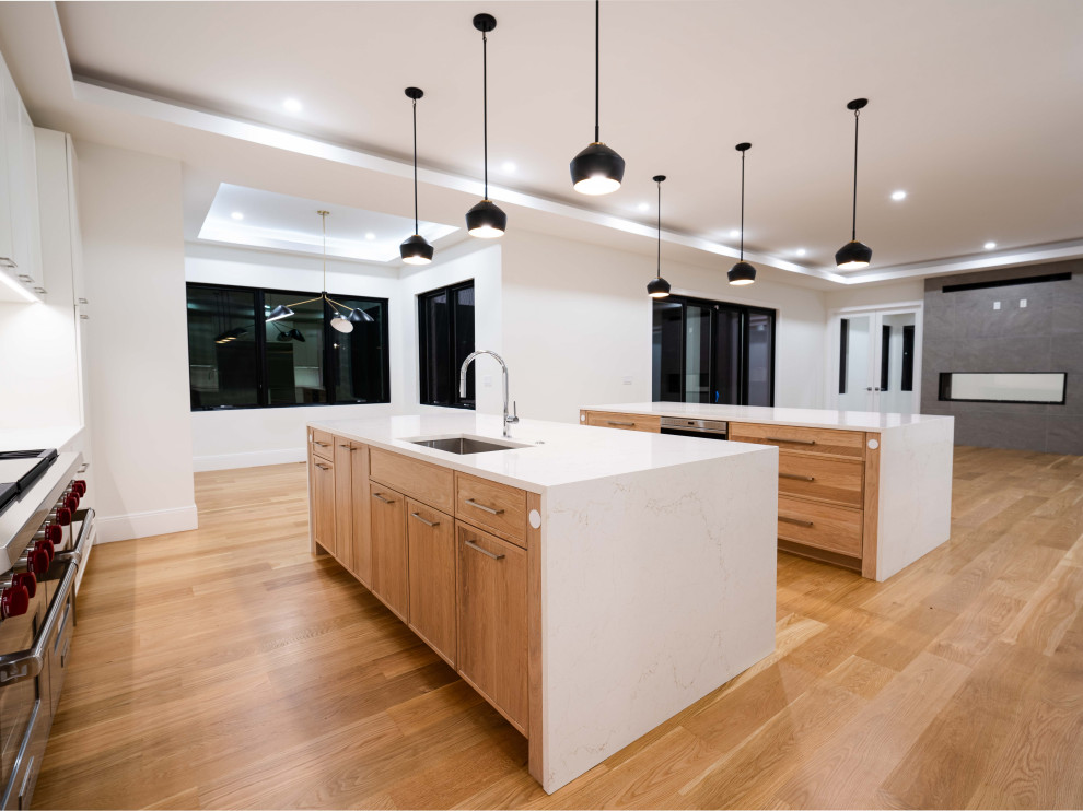 Example of a transitional light wood floor and tray ceiling kitchen design in Boston with an undermount sink, shaker cabinets, quartz countertops, quartz backsplash, stainless steel appliances and two islands