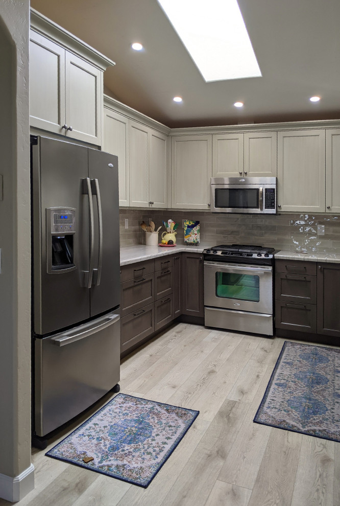 This is an example of a medium sized coastal u-shaped open plan kitchen in San Luis Obispo with a submerged sink, shaker cabinets, grey cabinets, engineered stone countertops, white splashback, glass tiled splashback, stainless steel appliances, light hardwood flooring, a breakfast bar, grey floors, white worktops and a vaulted ceiling.