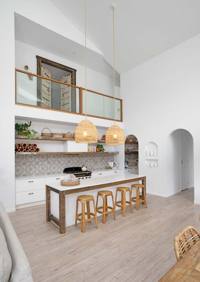 На фото: параллельная кухня-гостиная в средиземноморском стиле с плоскими фасадами, белыми фасадами, столешницей из кварцевого агломерата, полом из винила, островом, бежевым полом, белой столешницей и сводчатым потолком с
