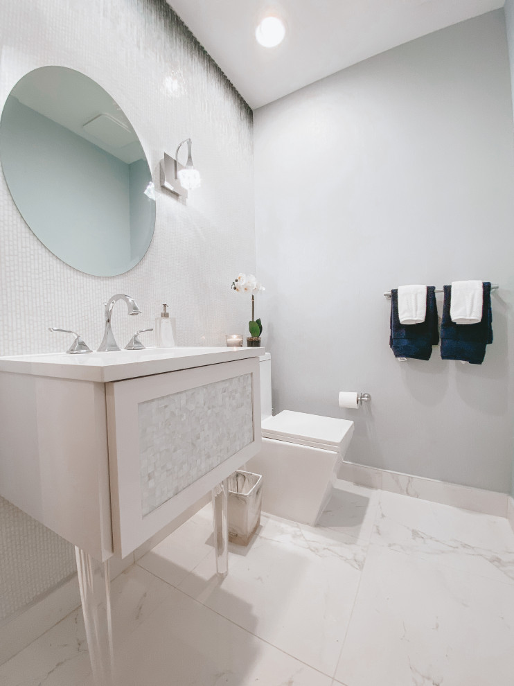 Пример оригинального дизайна: туалет в стиле модернизм с белыми фасадами, унитазом-моноблоком, разноцветной плиткой, плиткой мозаикой, полом из керамогранита, врезной раковиной, столешницей из искусственного камня, белым полом, белой столешницей, подвесной тумбой и обоями на стенах