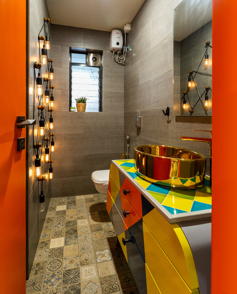 This is an example of a mid-sized eclectic 3/4 bathroom in Mumbai with brown walls, a vessel sink, a wall-mount toilet, gray tile, mosaic tile floors, beige floor, multi-coloured benchtops and flat-panel cabinets.