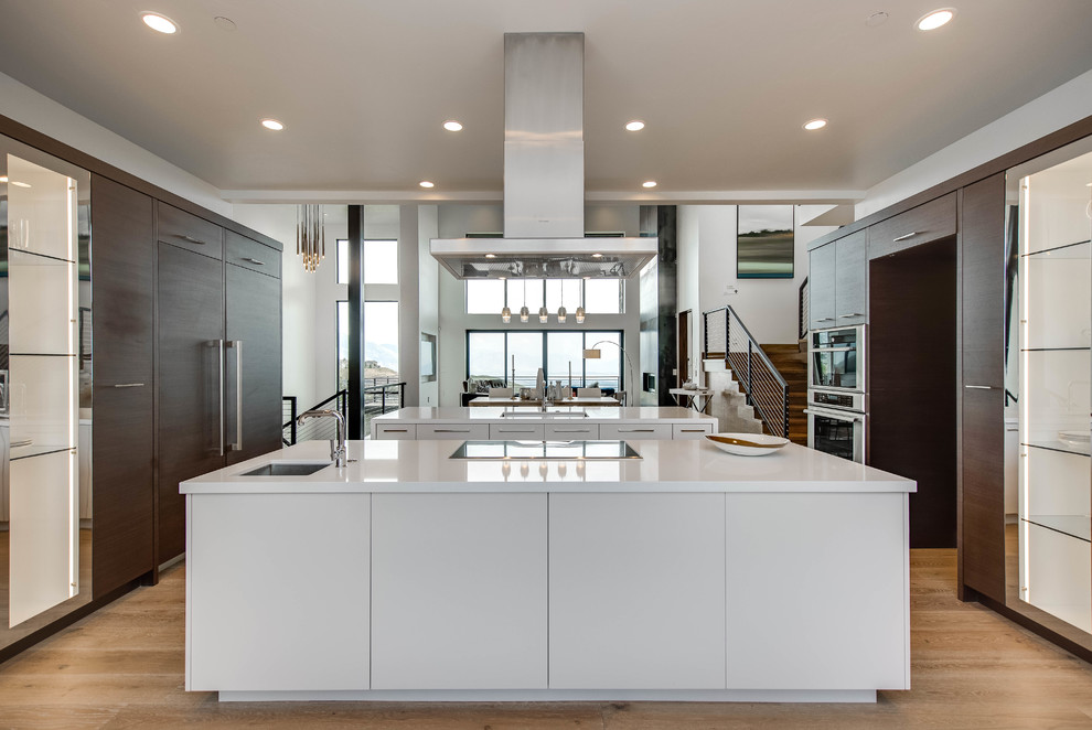 Photo of a large contemporary kitchen in Salt Lake City with a single-bowl sink, flat-panel cabinets, dark wood cabinets, solid surface benchtops, light hardwood floors and multiple islands.