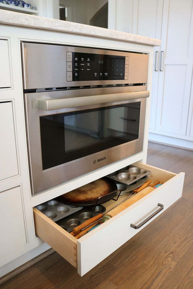 Example of a large transitional galley medium tone wood floor and brown floor enclosed kitchen design with a farmhouse sink, shaker cabinets, gray cabinets, quartzite countertops, beige backsplash, subway tile backsplash, stainless steel appliances and a peninsula