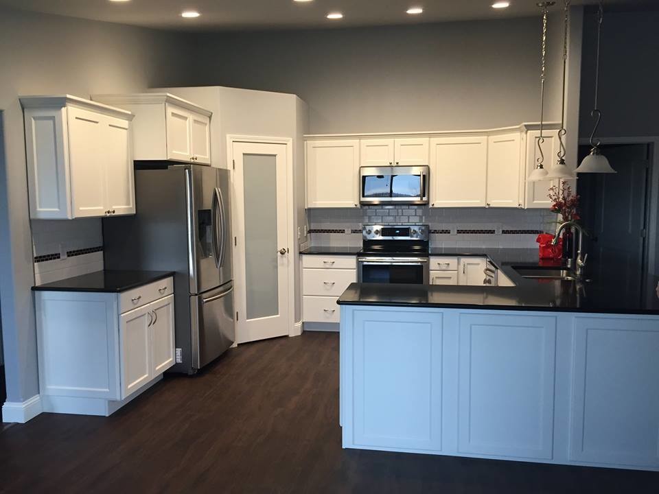 Example of a mid-sized transitional medium tone wood floor and brown floor kitchen design with an undermount sink, shaker cabinets, white cabinets, white backsplash, subway tile backsplash, stainless steel appliances and a peninsula