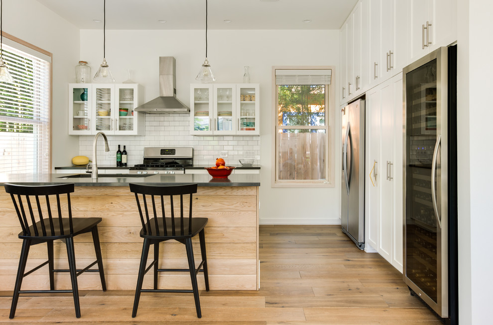 Transitional l-shaped kitchen in Austin with an undermount sink, shaker cabinets, white cabinets, white splashback, subway tile splashback, stainless steel appliances, medium hardwood floors, a peninsula and brown floor.