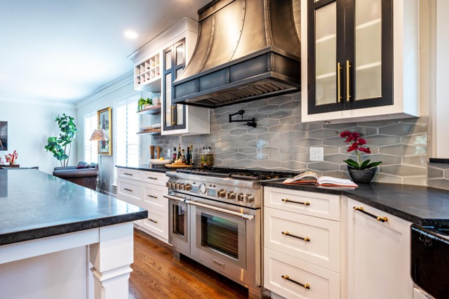 Mid-sized transitional medium tone wood floor and brown floor eat-in kitchen photo with a farmhouse sink, shaker cabinets, white cabinets, soapstone countertops, gray backsplash, porcelain backsplash, stainless steel appliances, an island and black countertops