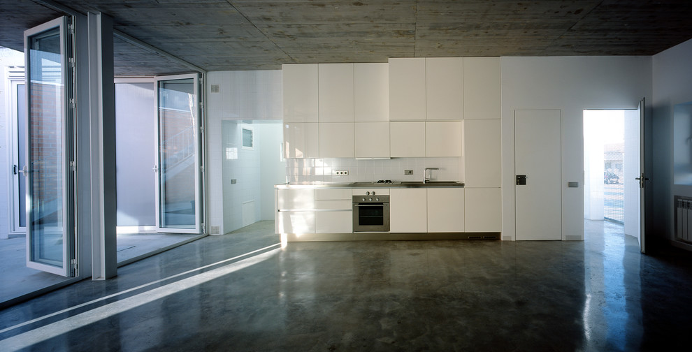 Example of a small minimalist single-wall concrete floor open concept kitchen design with flat-panel cabinets, white cabinets, stainless steel countertops, no island, white backsplash, porcelain backsplash and white appliances