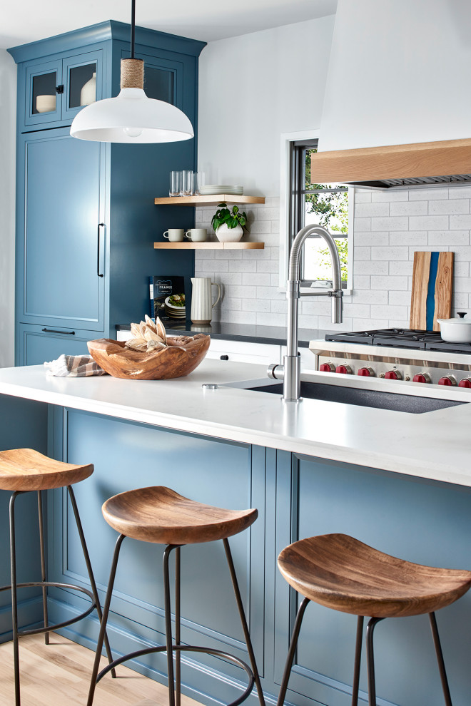 Immagine di una cucina tradizionale con lavello stile country, ante blu, paraspruzzi bianco, pavimento marrone, elettrodomestici in acciaio inossidabile, 2 o più isole e top bianco