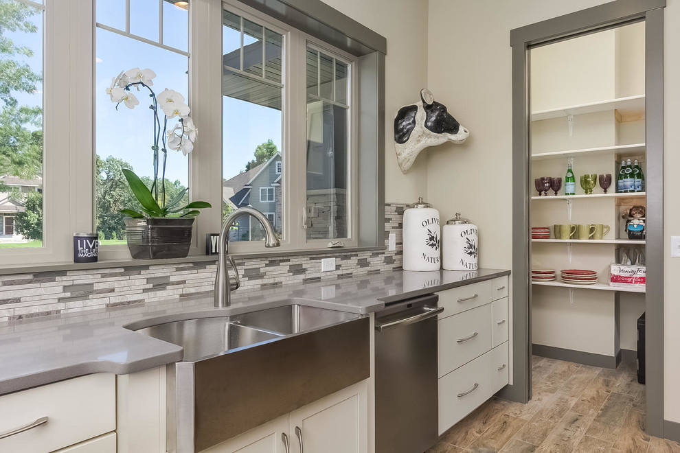 Photo of an arts and crafts u-shaped kitchen pantry in Minneapolis with a farmhouse sink, shaker cabinets, quartz benchtops, grey splashback, porcelain splashback, stainless steel appliances, porcelain floors and with island.