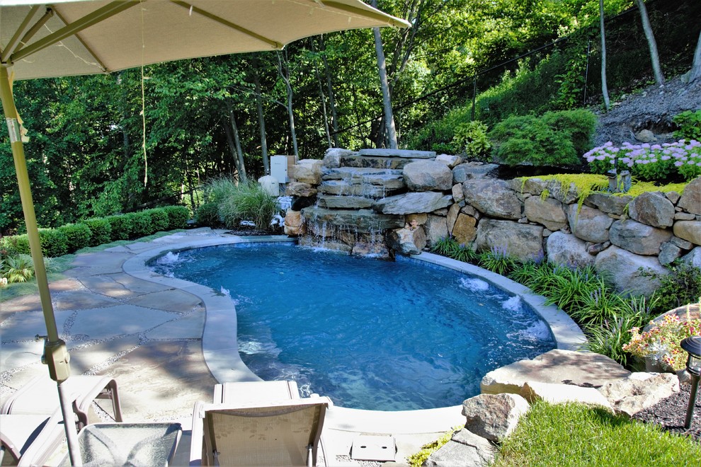 This is an example of a small country backyard kidney-shaped natural pool in New York with a water feature and natural stone pavers.