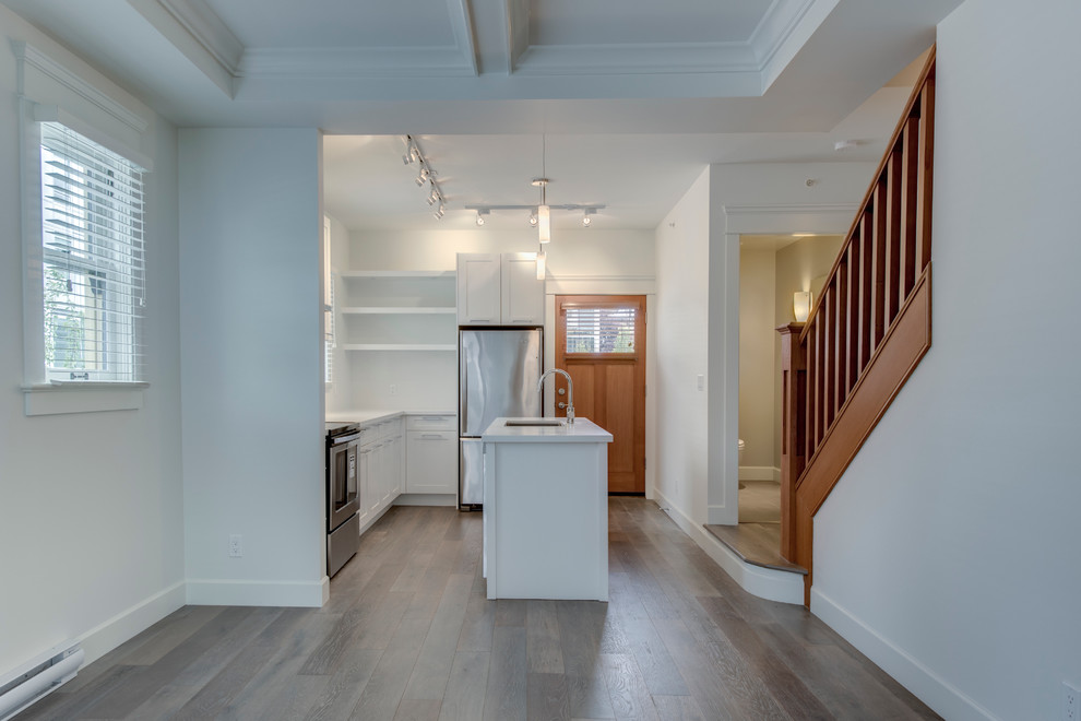 Inspiration for a mid-sized arts and crafts galley eat-in kitchen in Vancouver with a double-bowl sink, flat-panel cabinets, white cabinets, quartzite benchtops, white splashback, stainless steel appliances, light hardwood floors and with island.