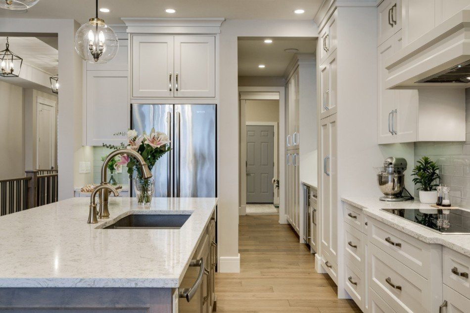 This is an example of a mid-sized traditional l-shaped eat-in kitchen in Calgary with an undermount sink, shaker cabinets, white cabinets, quartz benchtops, grey splashback, glass tile splashback, stainless steel appliances, light hardwood floors, with island, beige floor and white benchtop.