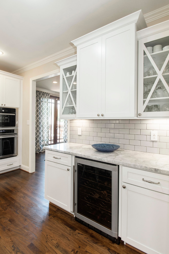 Photo of a large transitional u-shaped open plan kitchen in Dallas with an undermount sink, shaker cabinets, white cabinets, quartz benchtops, white splashback, porcelain splashback, stainless steel appliances, medium hardwood floors and with island.