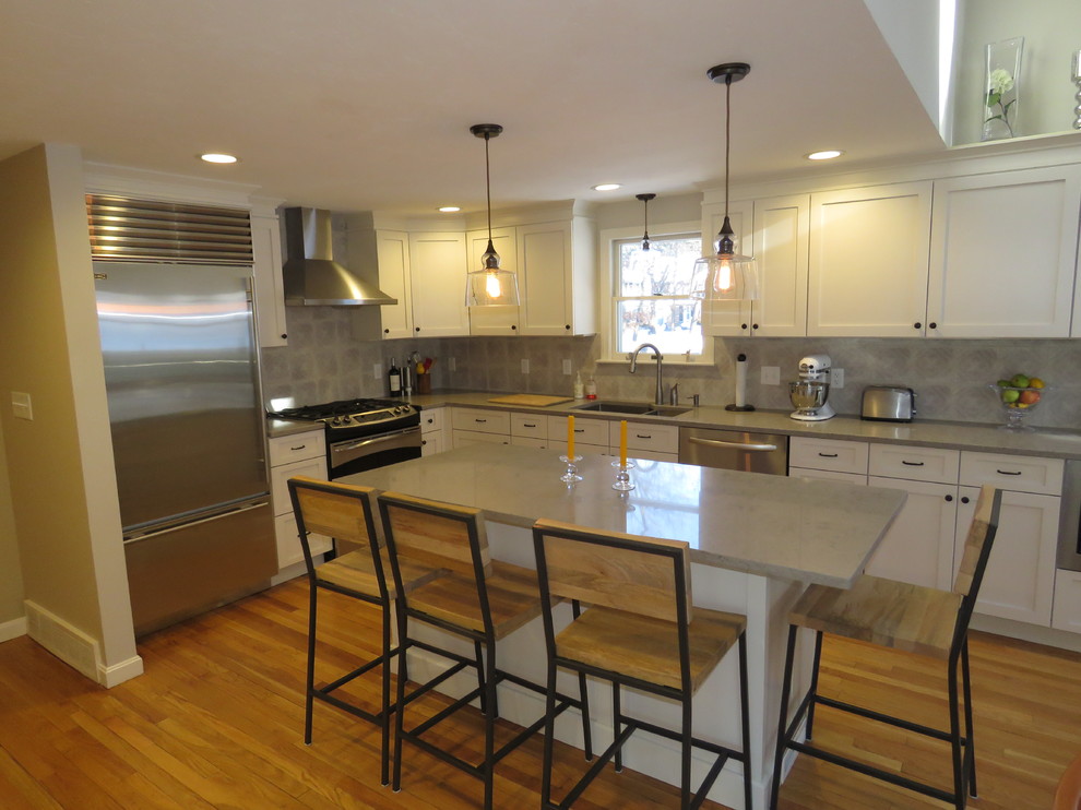Large transitional l-shaped medium tone wood floor open concept kitchen photo in Boston with an undermount sink, shaker cabinets, white cabinets, quartz countertops, gray backsplash, stainless steel appliances and an island