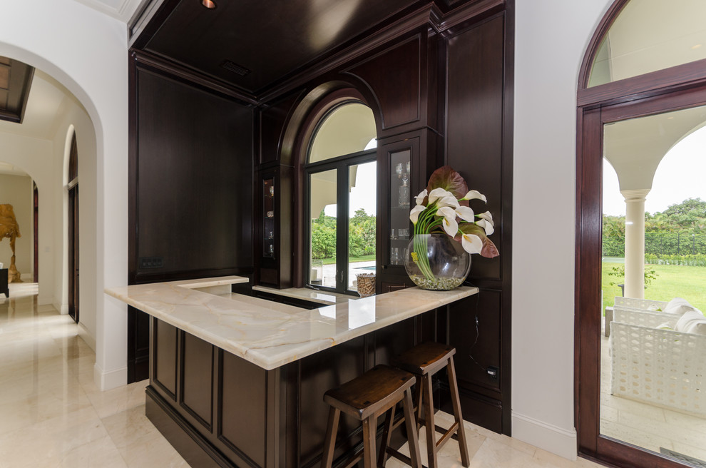 Photo of a mid-sized traditional u-shaped seated home bar in Miami with marble floors, recessed-panel cabinets and dark wood cabinets.