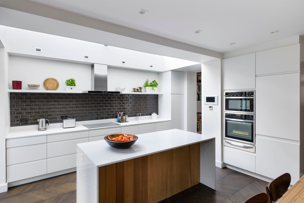 Inspiration for a contemporary l-shaped eat-in kitchen in London with flat-panel cabinets, black splashback, stainless steel appliances, dark hardwood floors and with island.