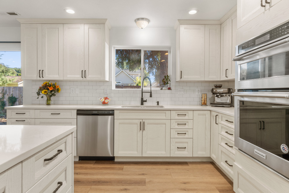 Medium sized contemporary kitchen/diner in Seattle with a double-bowl sink, shaker cabinets, white cabinets, engineered stone countertops, white splashback, porcelain splashback, stainless steel appliances, laminate floors, a breakfast bar, brown floors and white worktops.