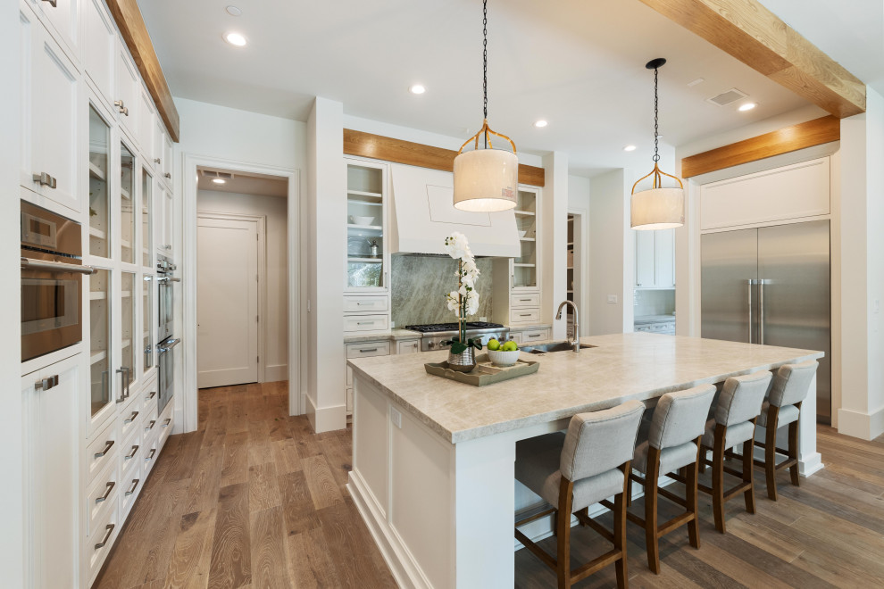 Huge transitional u-shaped medium tone wood floor, brown floor and exposed beam enclosed kitchen photo in Houston with an integrated sink, beaded inset cabinets, white cabinets, quartz countertops, gray backsplash, marble backsplash, stainless steel appliances, an island and beige countertops