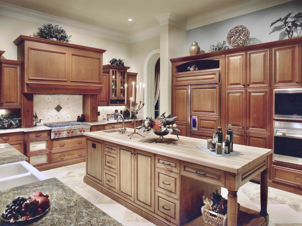 Example of a huge transitional u-shaped travertine floor and beige floor eat-in kitchen design in Miami with a farmhouse sink, raised-panel cabinets, medium tone wood cabinets, granite countertops, beige backsplash, travertine backsplash, stainless steel appliances, an island and multicolored countertops