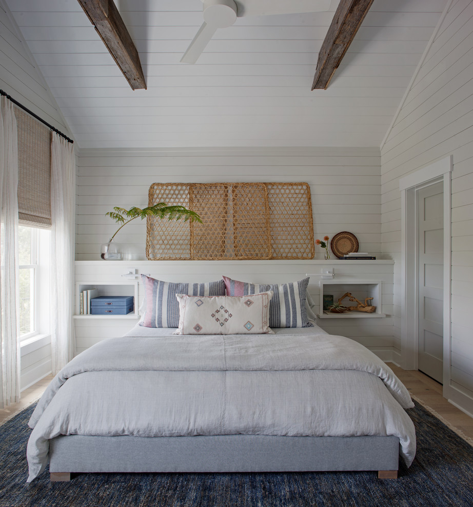 Large beach style master bedroom with white walls, light hardwood floors, no fireplace and brown floor.
