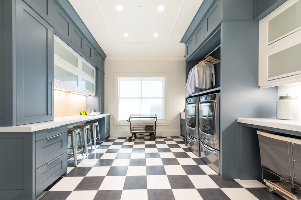 This is an example of an expansive transitional galley utility room in Salt Lake City with a farmhouse sink, a side-by-side washer and dryer, shaker cabinets, marble benchtops, white walls, multi-coloured floor, white benchtop and blue cabinets.