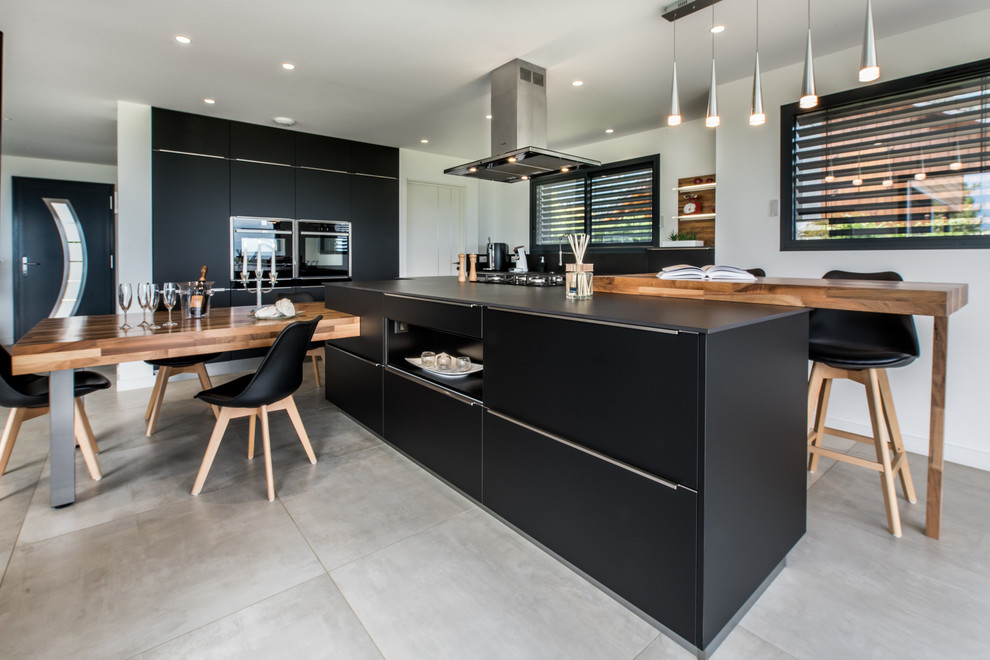 This is an example of a large modern galley open plan kitchen in Grenoble with an undermount sink, beaded inset cabinets, black cabinets, granite benchtops, black splashback, panelled appliances, ceramic floors, with island, grey floor and black benchtop.