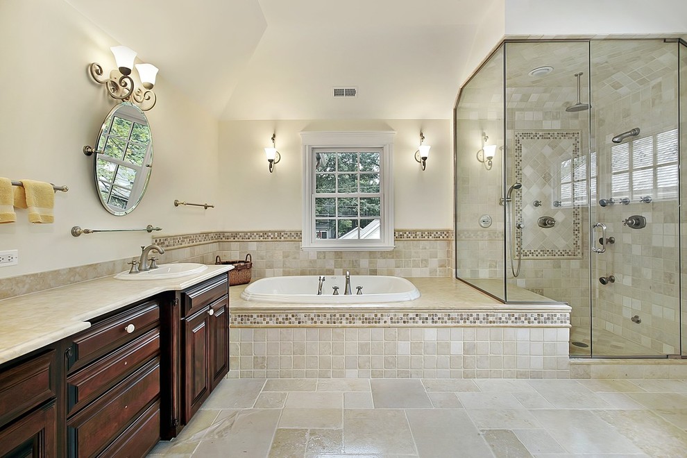 Large traditional 3/4 bathroom in Other with furniture-like cabinets, dark wood cabinets, a drop-in tub, a corner shower, beige tile, gray tile, multi-coloured tile, white tile, a drop-in sink and a hinged shower door.