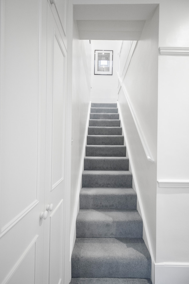 This is an example of a small traditional carpeted l-shaped staircase in London with carpet risers and wood railing.