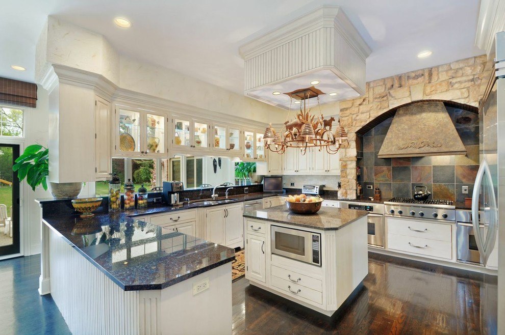 This is an example of a large traditional u-shaped eat-in kitchen in Chicago with beaded inset cabinets, white cabinets, granite benchtops, multi-coloured splashback, slate splashback, stainless steel appliances, dark hardwood floors, with island, brown floor, a double-bowl sink and black benchtop.