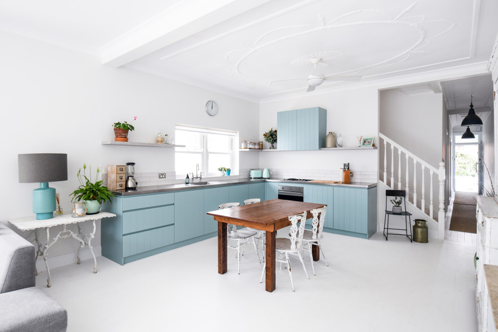 Inspiration for a small beach style l-shaped eat-in kitchen in Sydney with an undermount sink, blue cabinets, stainless steel benchtops, white splashback, subway tile splashback, stainless steel appliances, light hardwood floors, no island, white floor and grey benchtop.