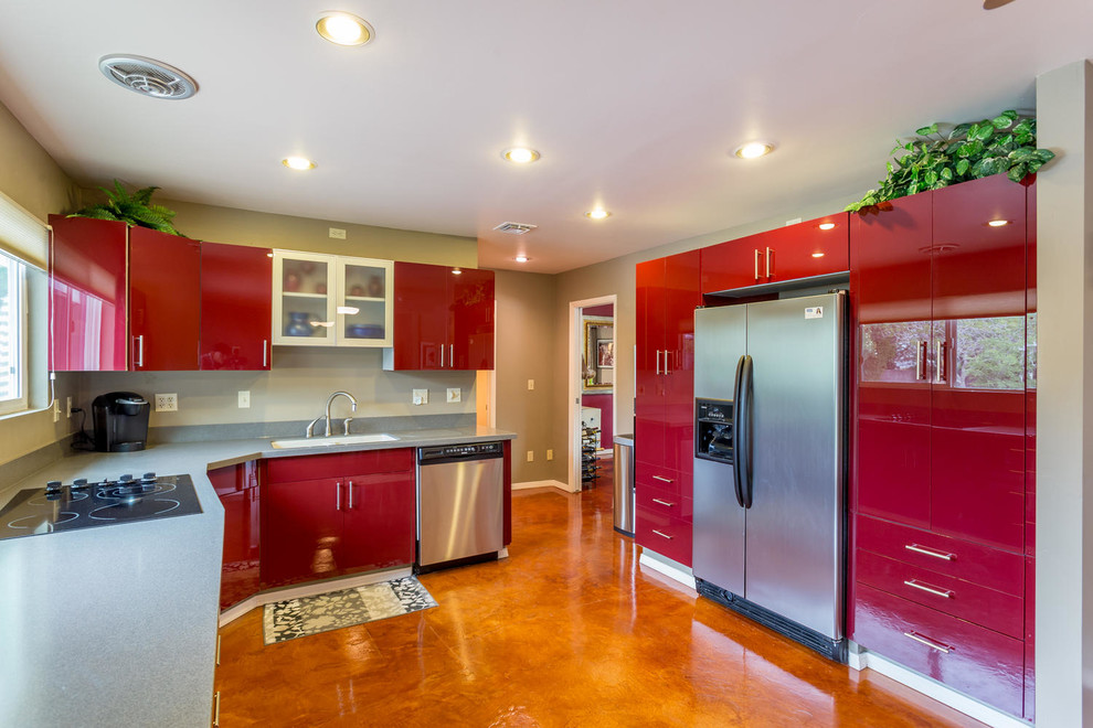 Large modern l-shaped open plan kitchen in Las Vegas with an integrated sink, flat-panel cabinets, red cabinets, solid surface benchtops, grey splashback, cement tile splashback, stainless steel appliances, concrete floors and no island.