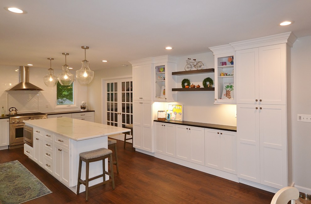 This is an example of an expansive transitional u-shaped eat-in kitchen in Philadelphia with an undermount sink, recessed-panel cabinets, white cabinets, quartz benchtops, white splashback, subway tile splashback, stainless steel appliances, vinyl floors, with island, brown floor and white benchtop.