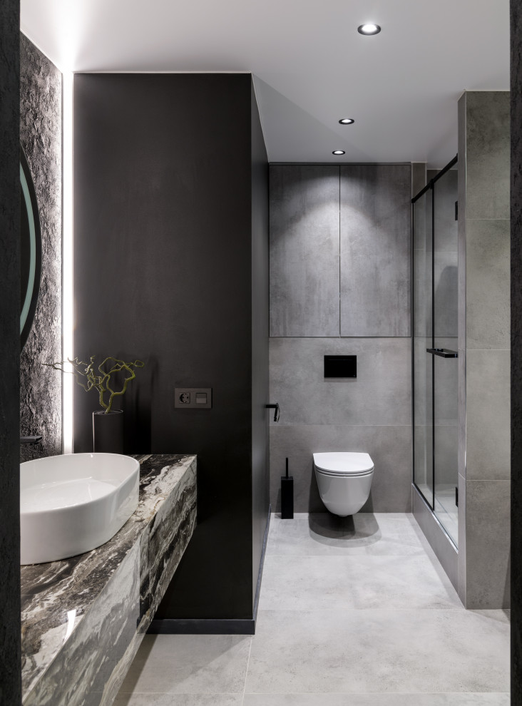 Inspiration for a large contemporary 3/4 bathroom in Novosibirsk with flat-panel cabinets, grey cabinets, an undermount tub, an alcove shower, a wall-mount toilet, gray tile, porcelain tile, black walls, porcelain floors, a drop-in sink, tile benchtops, grey floor, a hinged shower door, grey benchtops, a single vanity and a floating vanity.