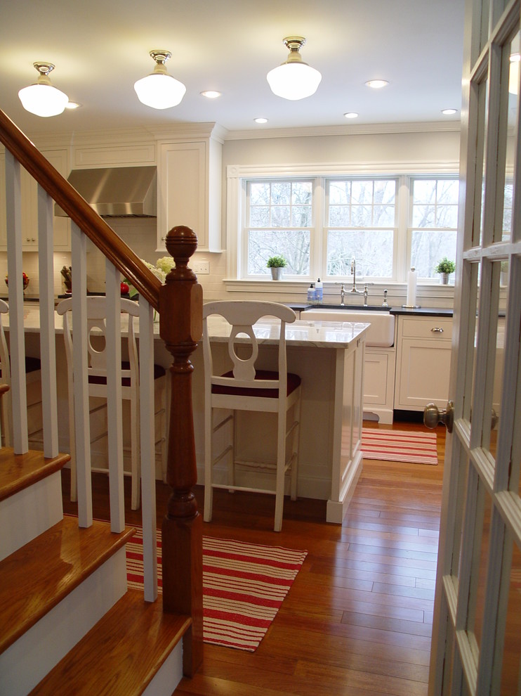 Enclosed kitchen - transitional enclosed kitchen idea in Boston with a farmhouse sink, recessed-panel cabinets, white cabinets, granite countertops, white backsplash, subway tile backsplash, stainless steel appliances and an island