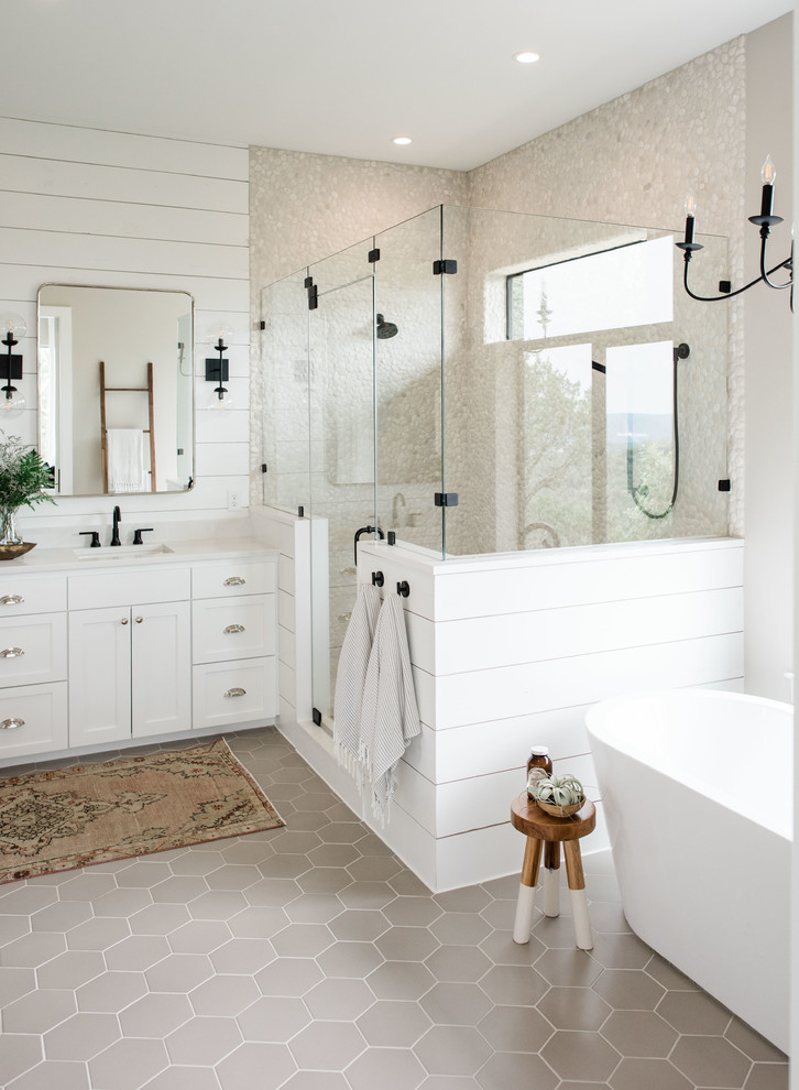 Inspiration for a large transitional master bathroom in Austin with shaker cabinets, white cabinets, a freestanding tub, a double shower, beige tile, pebble tile, grey walls, porcelain floors, an undermount sink, quartzite benchtops, grey floor, a hinged shower door and white benchtops.