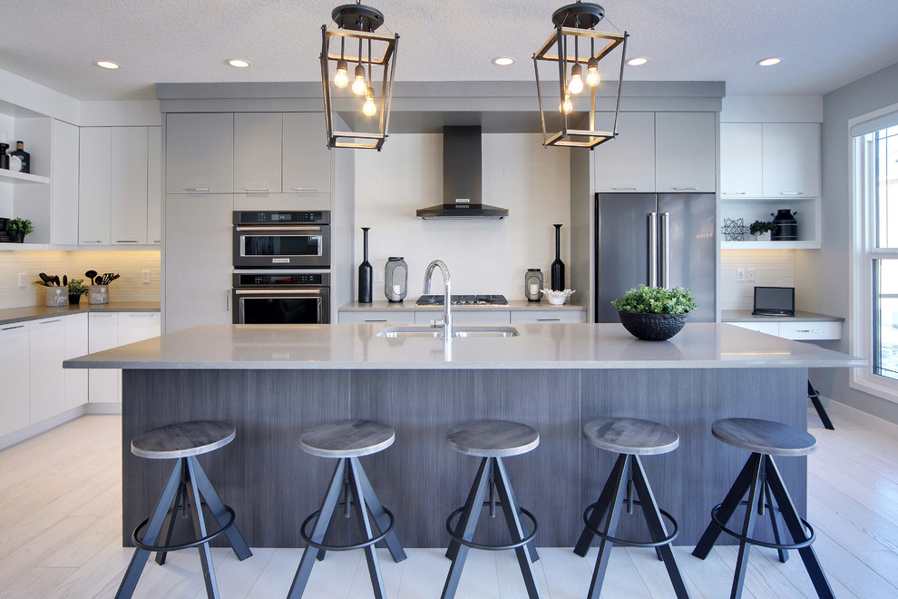 Contemporary l-shaped kitchen in Calgary with an undermount sink, flat-panel cabinets, grey cabinets, white splashback, stainless steel appliances, light hardwood floors, with island and beige floor.
