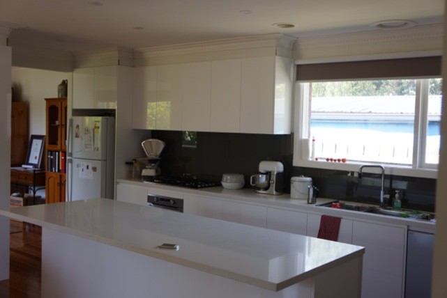 Large modern galley eat-in kitchen in Melbourne with flat-panel cabinets, white cabinets, quartz benchtops, black splashback, glass sheet splashback, stainless steel appliances, with island, a double-bowl sink, medium hardwood floors and white benchtop.